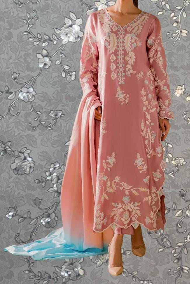 A woman wearing a pink dress with intricate floral embroidery stands against a gray floral background.