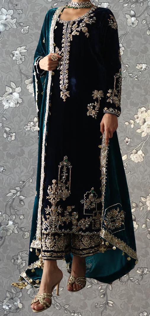 A person wearing an ornate, intricately embroidered black dress with gold accents, standing against a floral patterned background.