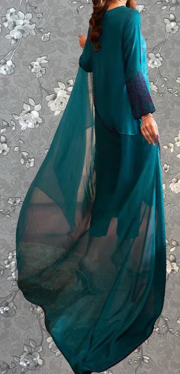 A woman wearing a long, flowing teal dress with a matching cape, standing against a gray floral background.