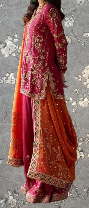 A woman wearing a vibrant red and orange traditional Indian outfit with intricate embroidery and patterns.