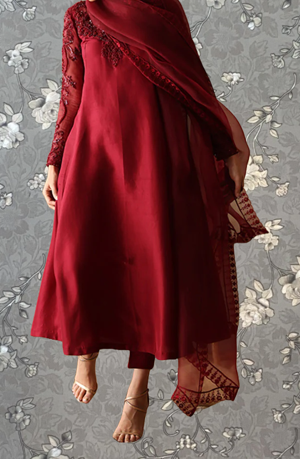 A woman wearing a long red dress with lace sleeves and a matching red shawl, standing against a gray floral background.