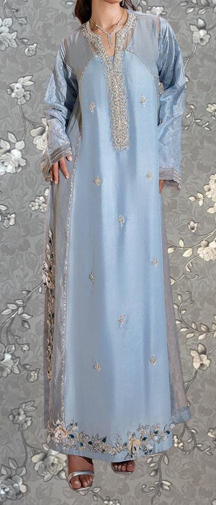 A woman wearing a long, light blue dress with intricate embroidery and floral patterns.
