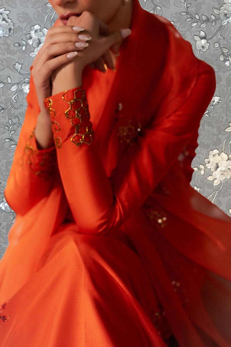 A close-up of a person wearing a vibrant red dress with gold embellishments, sitting with their hands on their chin.