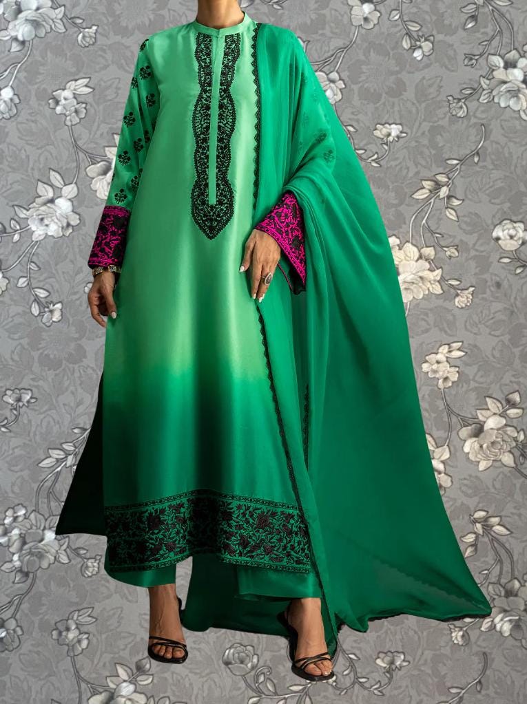 A person wearing a long green dress with pink accents, standing against a gray floral background.