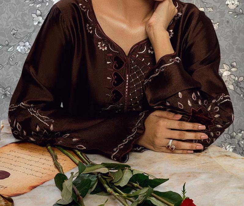 A woman in a brown dress with a floral pattern is sitting at a table with a bouquet of flowers and a piece of paper.