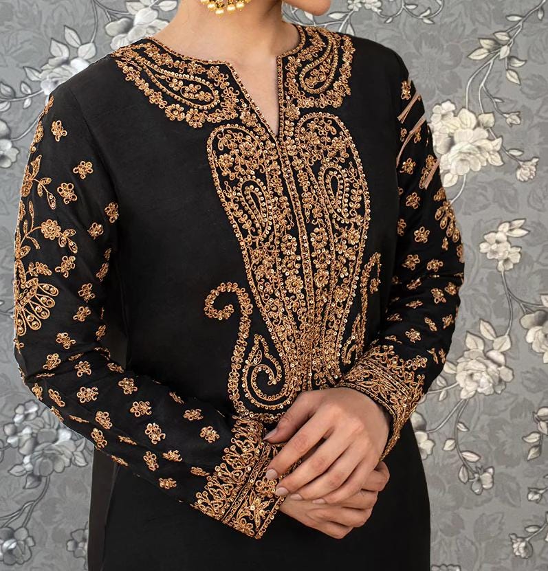 A woman wearing a black dress with gold embroidered patterns on the sleeves and collar.