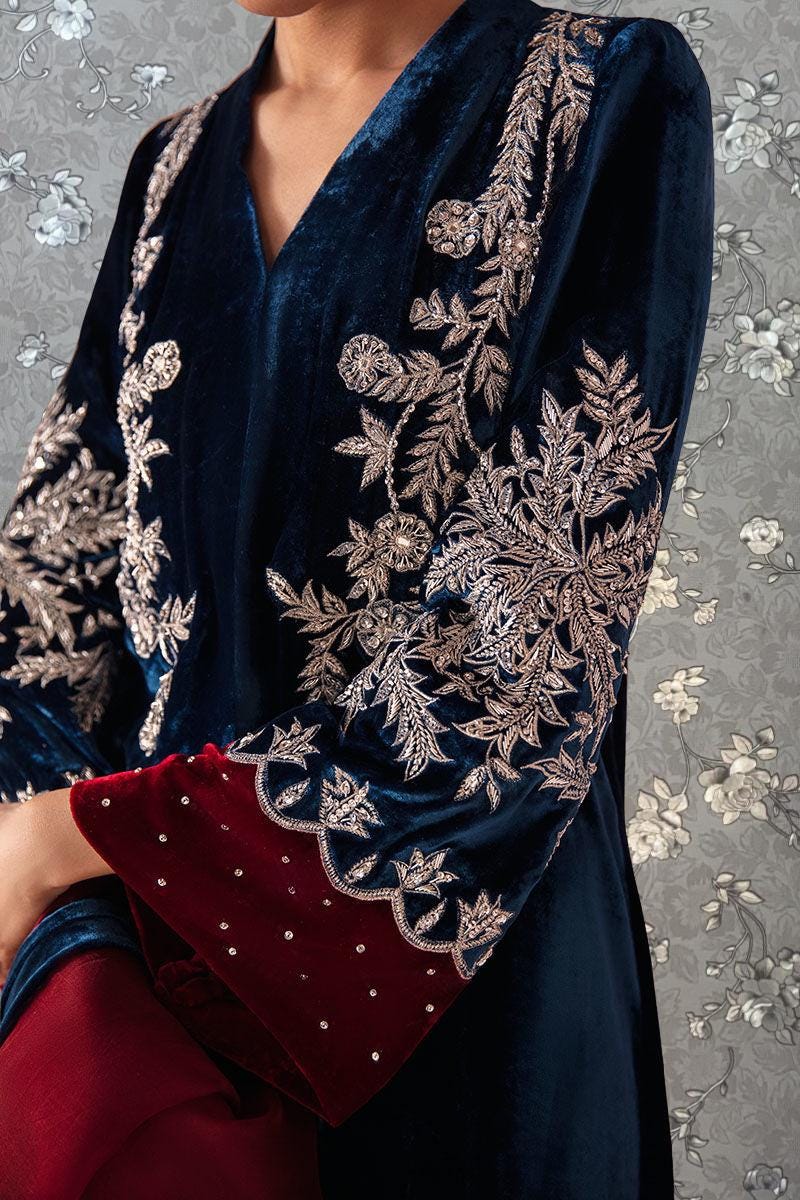 A close-up of a person wearing a blue velvet jacket with intricate gold embroidery on the sleeves and collar.