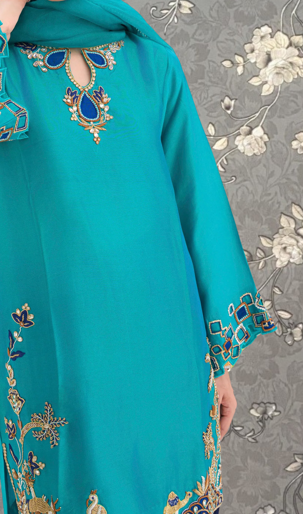 A close-up view of a turquoise dress with intricate embroidered designs, including floral patterns and geometric shapes.