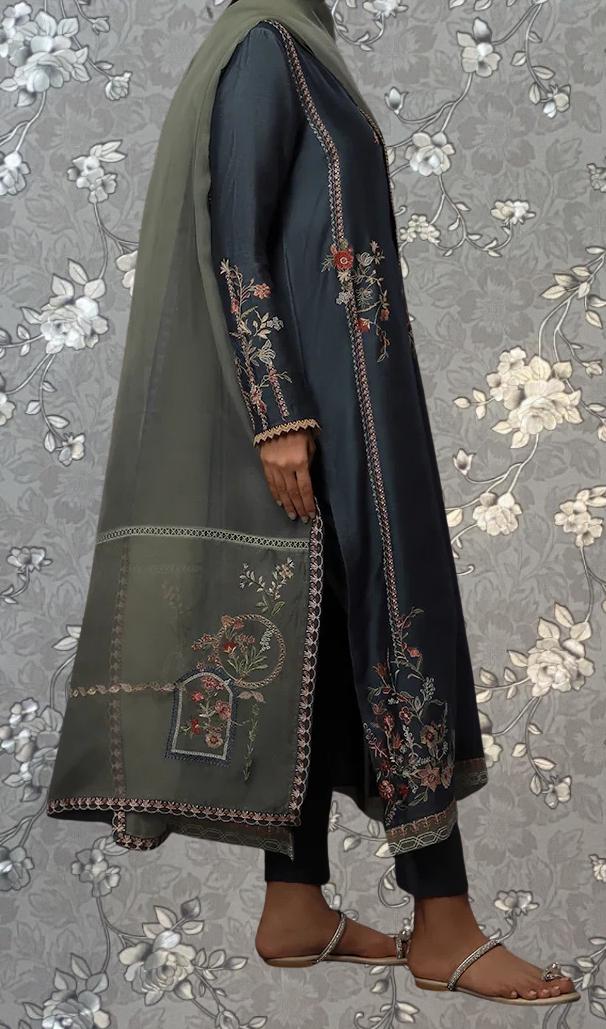 A person wearing a long, dark blue dress with intricate embroidered patterns on the sleeves and hem. The dress has a green shawl draped over the shoulders, and the person is wearing brown sandals.