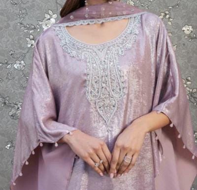 A woman wearing a pink dress with intricate embroidery and a matching pink shawl stands against a gray floral background.