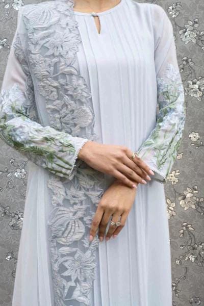 A person wearing a long, light blue dress with intricate floral embroidery on the sleeves and collar.