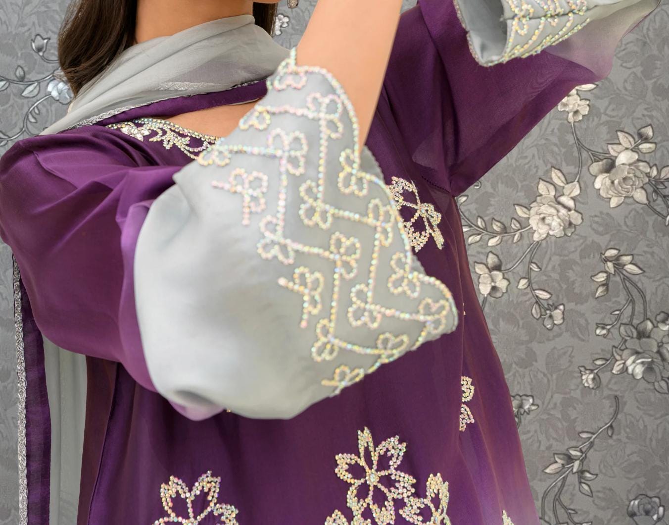 A close-up view of a person wearing a purple and gray dress with intricate embroidered patterns.