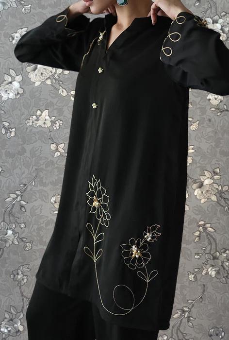 A person wearing a black dress with gold embroidered flowers on the front.