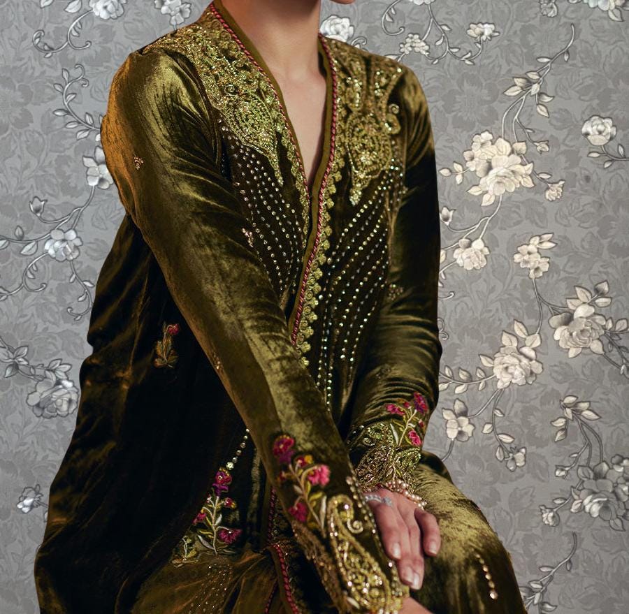 A person wearing a long, gold and green velvet dress with intricate embroidery and floral patterns.