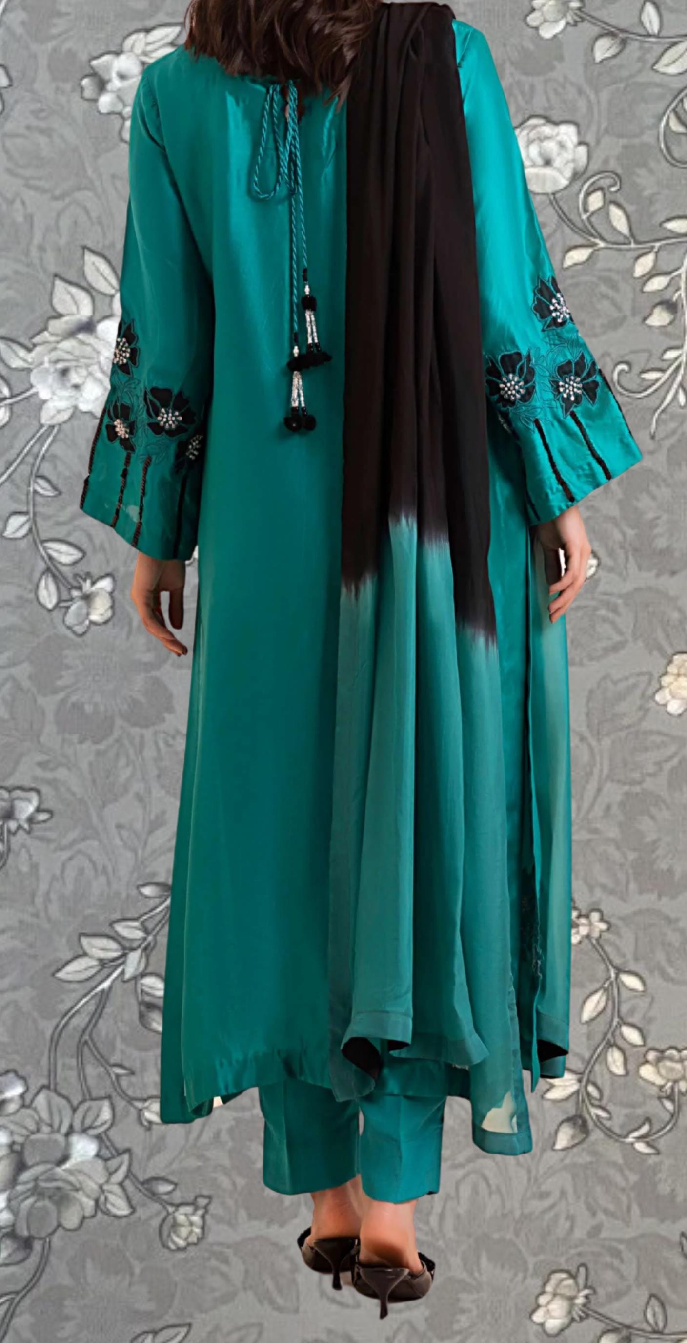 A person wearing a long, teal-colored dress with black accents, including a scarf draped over the shoulder.