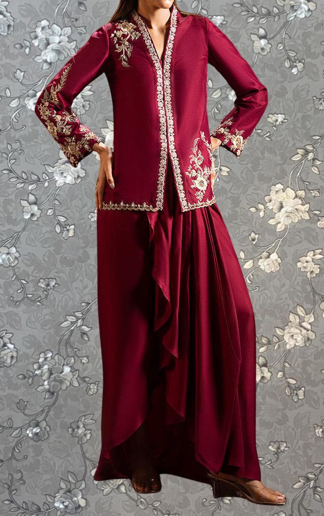 A woman wearing a long, burgundy dress with intricate embroidery and a high collar, standing against a gray floral background.