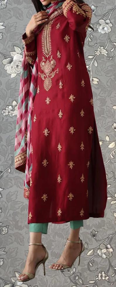 A woman wearing a red and gold embroidered dress with a floral pattern, standing against a gray floral background.