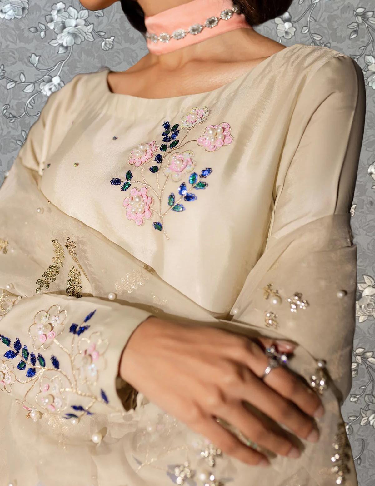 A close-up of a person wearing a beige dress with intricate floral embroidery on the front.