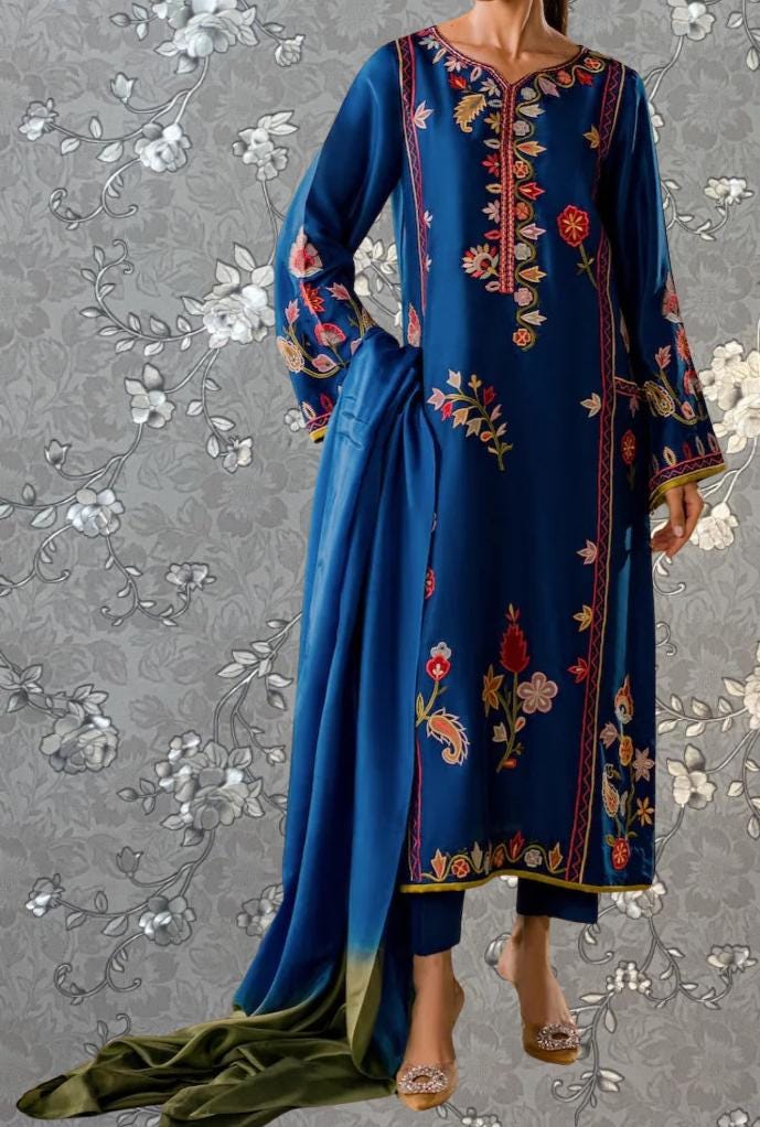 A woman wearing a blue dress with intricate floral embroidery and a matching blue shawl.