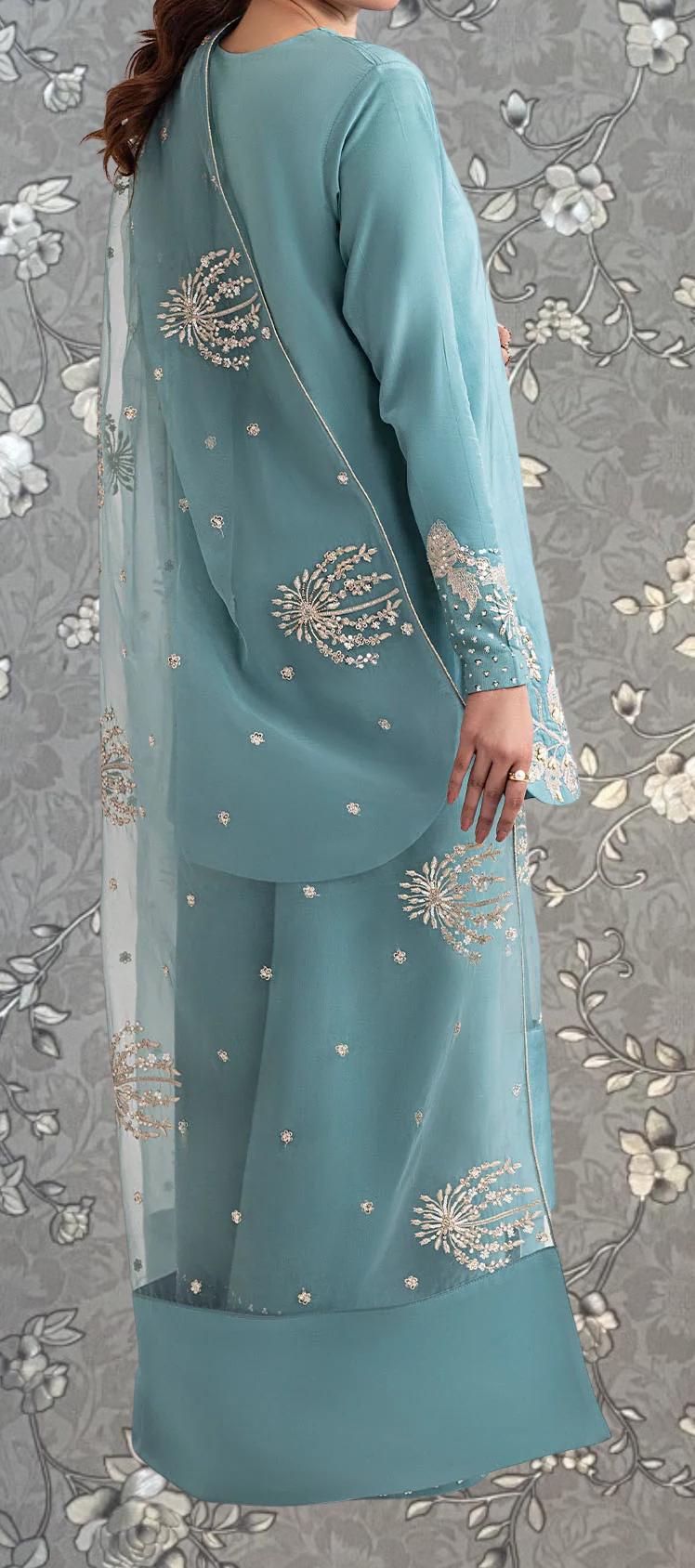 A woman wearing a long, light blue dress with intricate embroidered designs on the back and skirt.