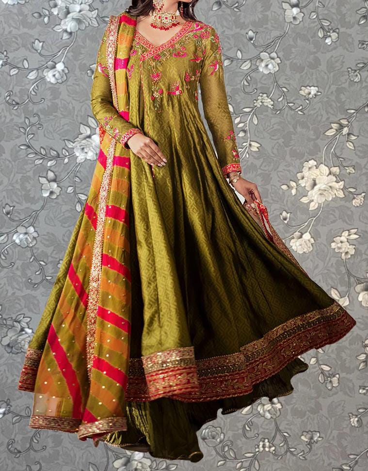 A woman wearing a long, green dress with a red and gold border, posing against a gray floral background.