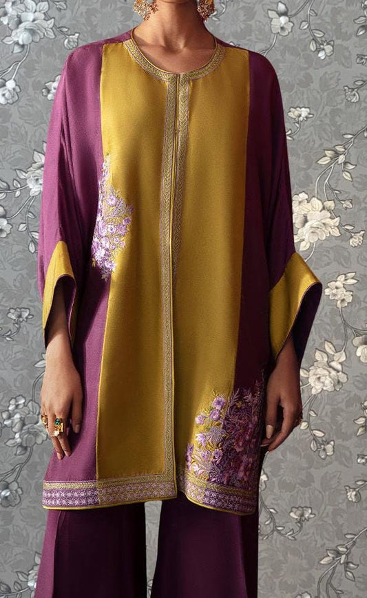A person wearing a colorful, patterned dress with a yellow and purple color scheme, standing against a floral background.
