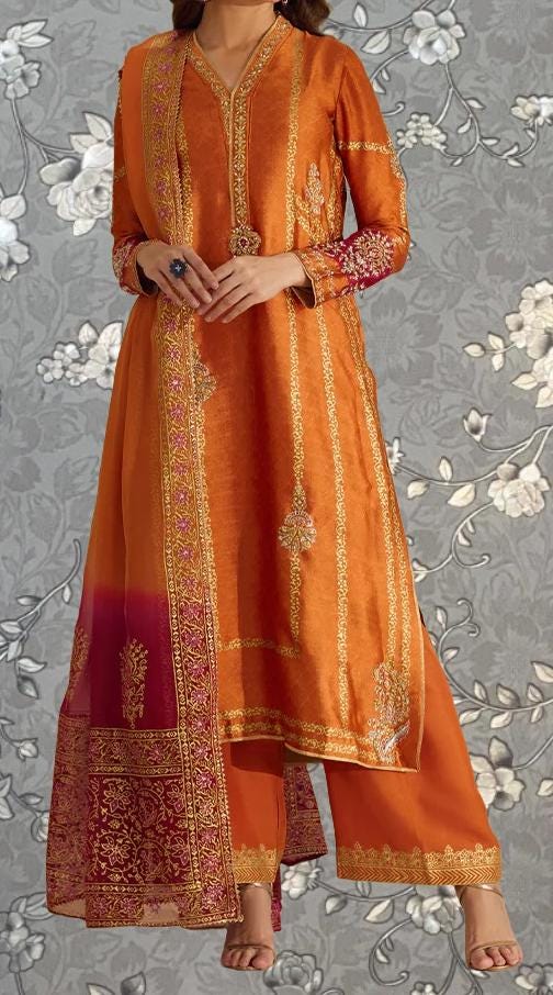 A woman wearing an orange and gold traditional Indian outfit with intricate embroidery and patterns.