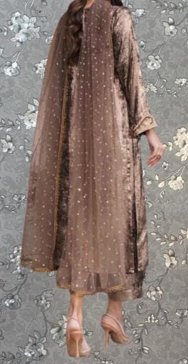 a woman wearing a long, brown dress with a sheer, polka-dotted pattern. She is standing against a gray floral background, and her back is facing the camera.