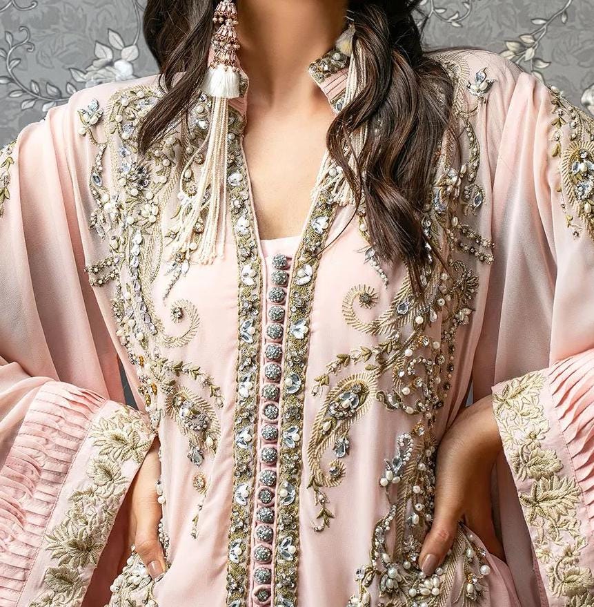A close-up of a woman wearing an ornate, pink dress with intricate embroidery and embellishments.