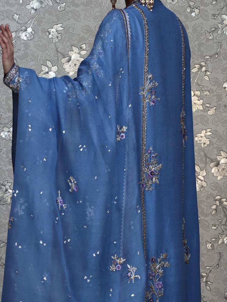 a person wearing a blue dress with intricate embroidered designs, including flowers and leaves, on the back.