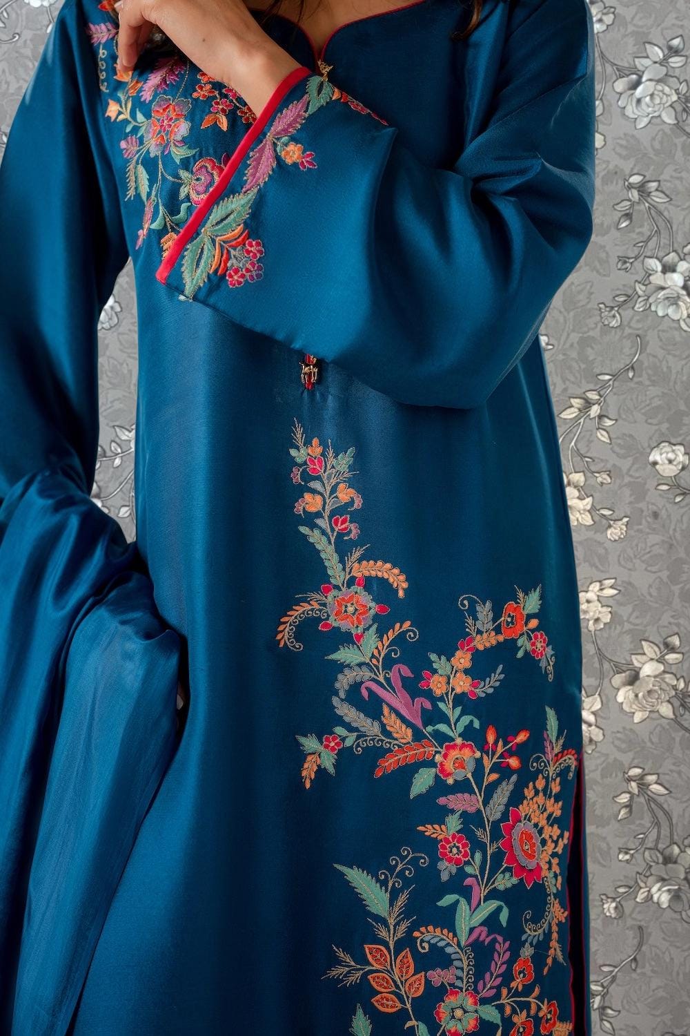 A close-up view of a person wearing a blue dress with intricate floral embroidery on the sleeves and hem.