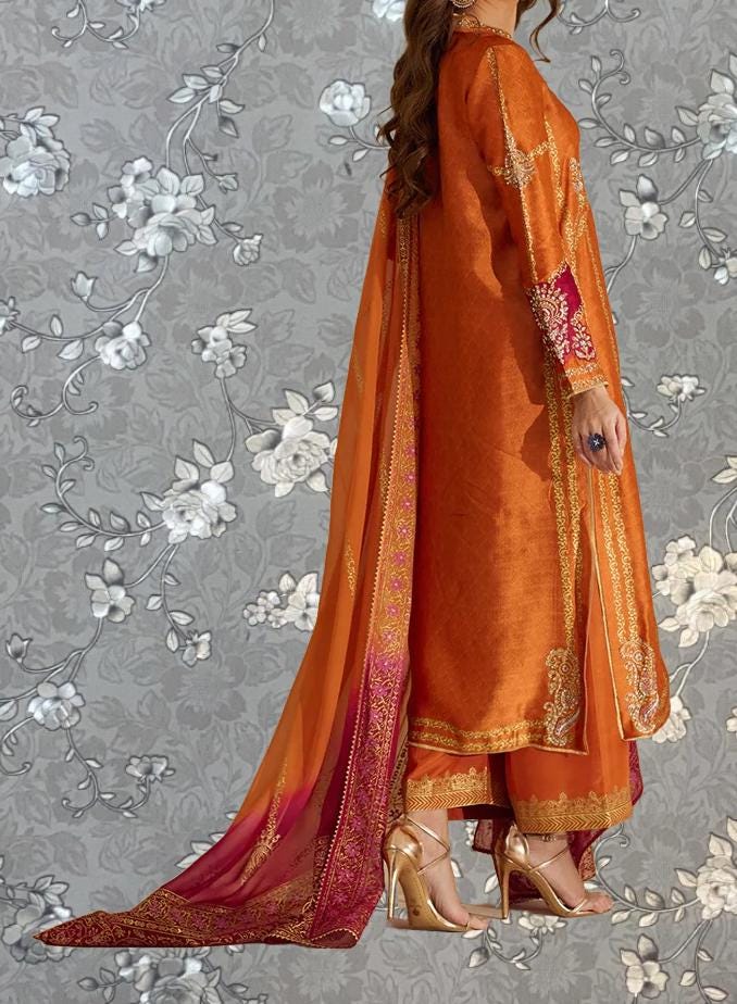 A woman wearing an orange and gold dress with a long train, standing against a gray floral background.