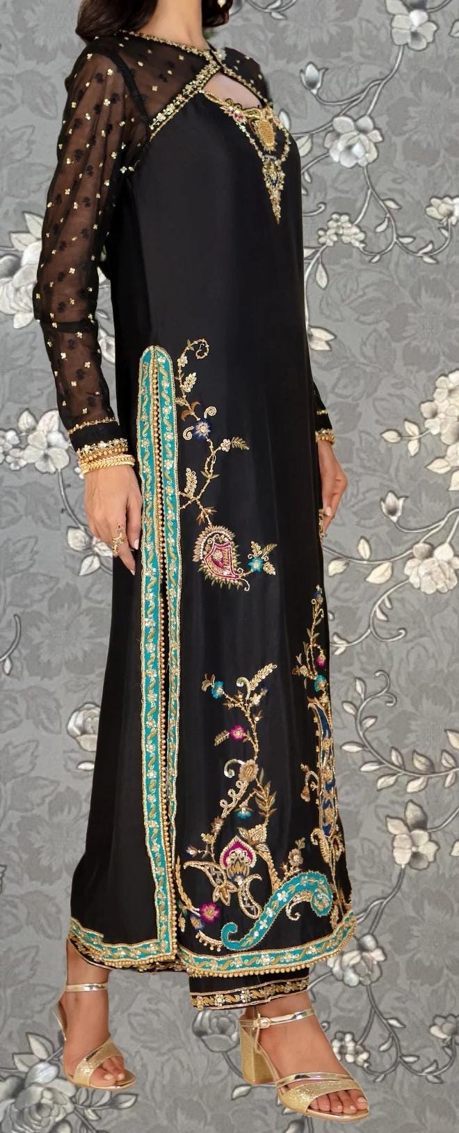 A woman wearing a long black dress with intricate gold embroidery and floral designs.