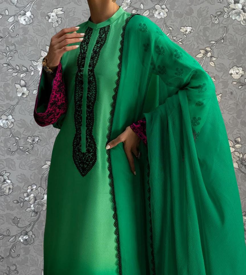 A person wearing a green dress with a matching green shawl and pink accents, posing against a gray floral background.
