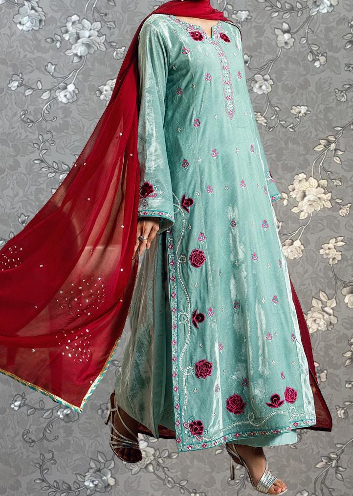 A woman wearing a long, light blue dress with red floral embroidery and a matching red shawl.