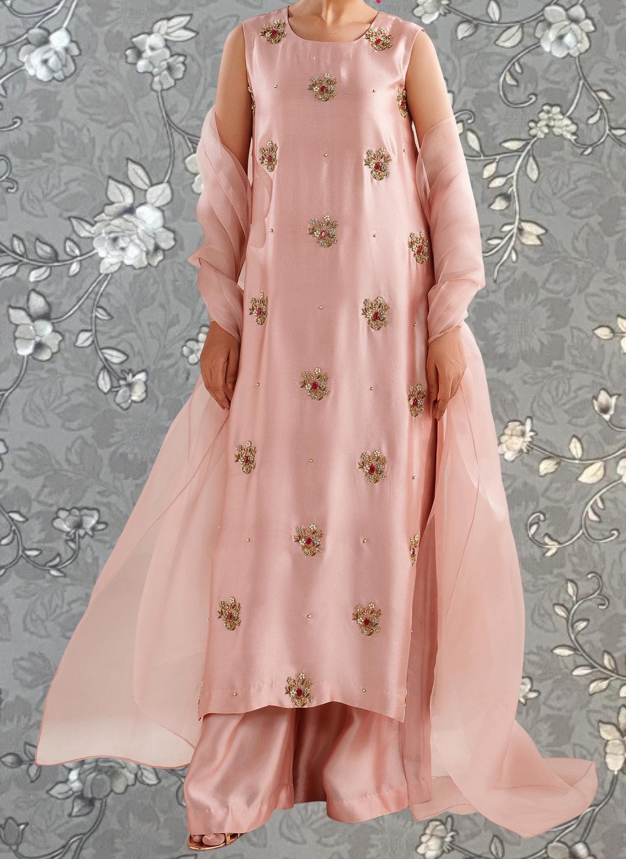 A woman wearing a pink dress with floral embroidery and a matching pink shawl.