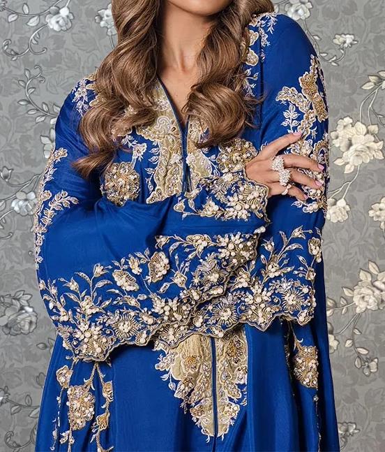 A woman wearing a blue dress with intricate gold embroidery and a long sleeve blouse.