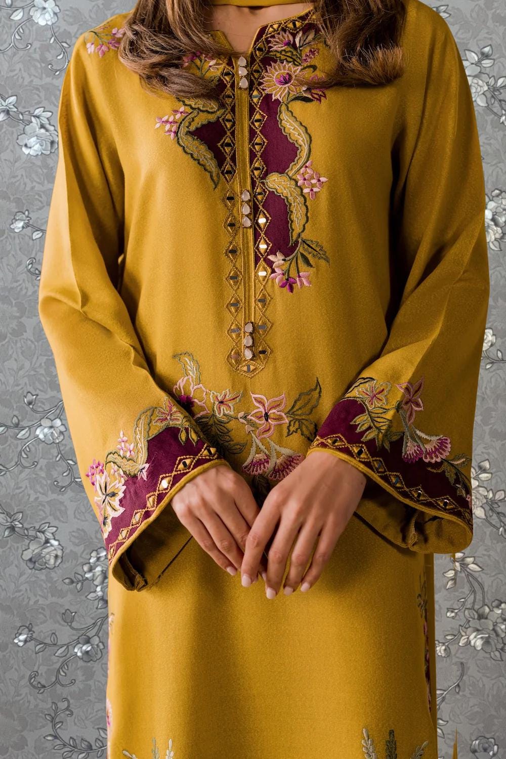 A close-up of a person wearing a yellow dress with intricate embroidered designs on the sleeves and collar.