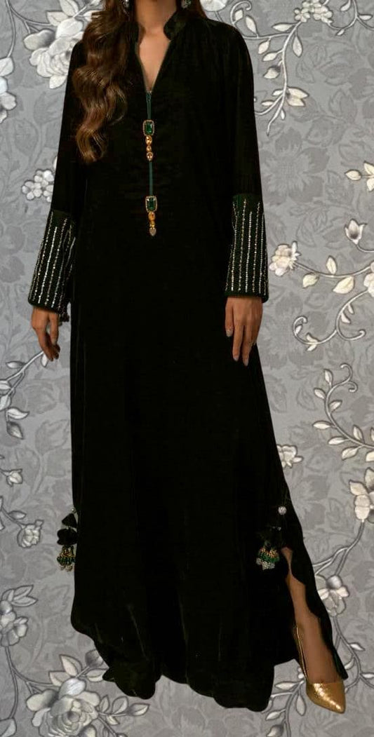 A woman wearing a long black dress with gold accents and tassels, standing against a gray floral background.