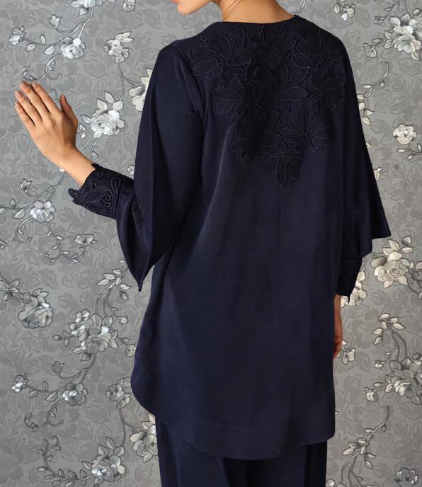 A person wearing a navy blue dress with a floral embroidered back stands against a gray floral background.