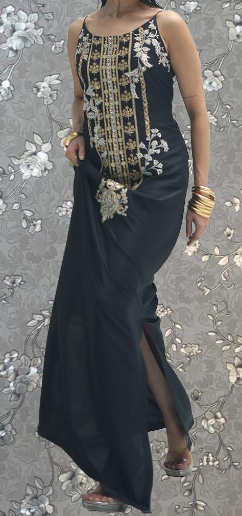 A woman wearing a long black dress with gold embroidery stands against a floral patterned background.