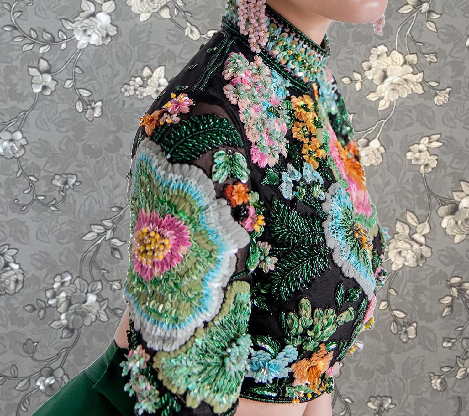 A close-up of a person wearing a black blouse with a floral pattern and colorful embroidery.