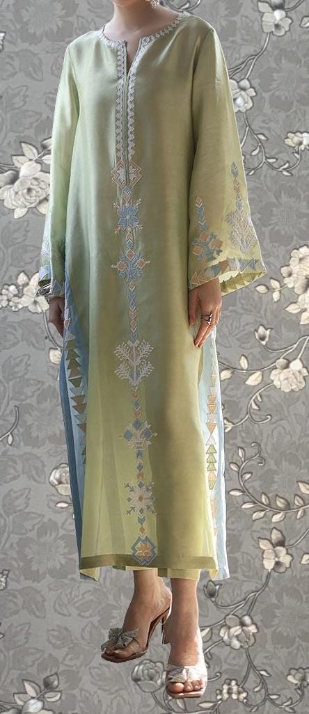 A person wearing a long, green dress with intricate embroidered patterns on the sleeves and hem.