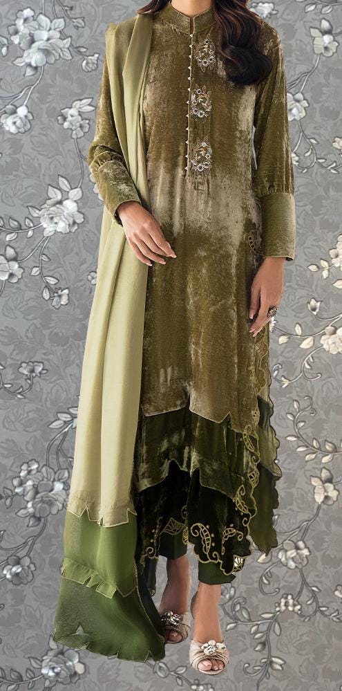 A woman wearing a green and gold dress with a long shawl, standing against a gray floral background.