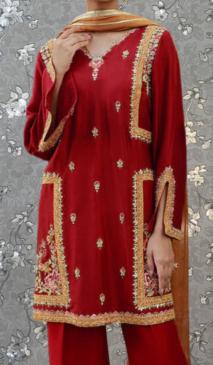 A person wearing a red and gold embroidered dress with a matching scarf.