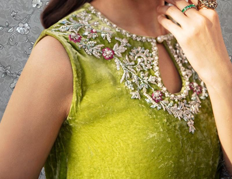 A close-up of a woman wearing a green dress with intricate embroidery and jewelry.