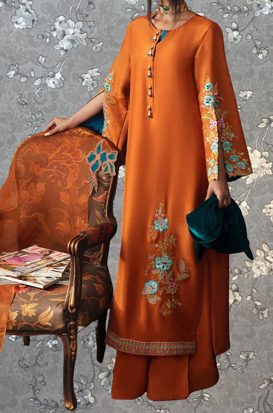 a woman wearing an orange dress with floral embroidery, standing next to a chair with a floral pattern. She is holding a green bag in her hand.