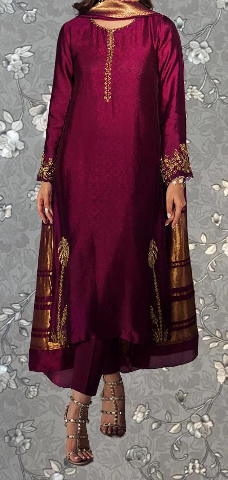 A woman wearing a long, burgundy dress with gold embroidery and a matching gold and gold shawl. She is wearing strappy sandals and has her hands in her pockets.