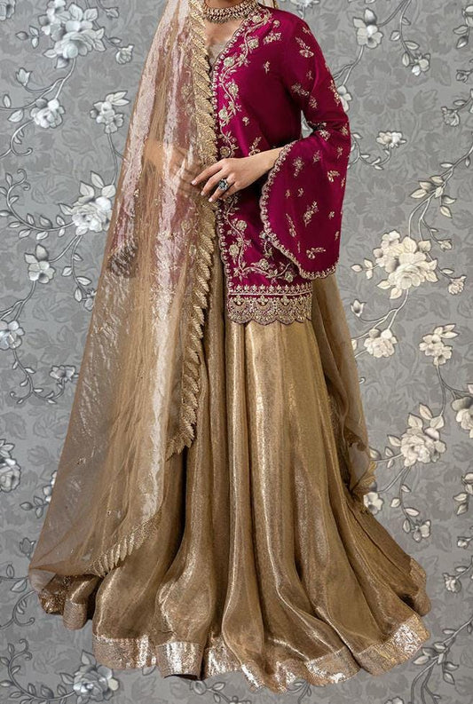 A woman wearing a long, gold and red dress with a matching gold and red shawl, standing against a gray floral background.