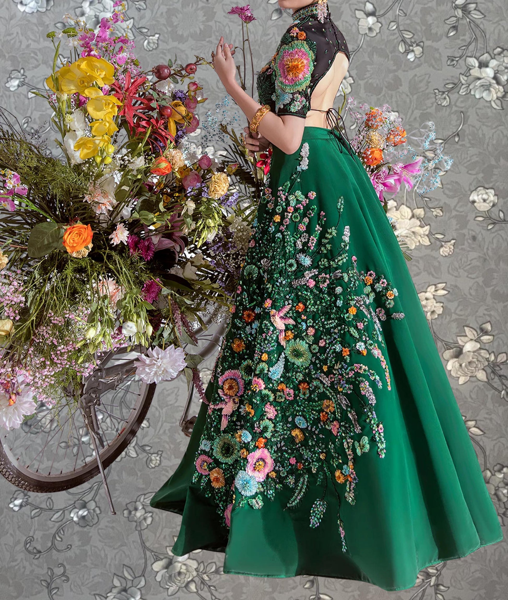 A woman wearing a green dress with a floral pattern is standing next to a bicycle with a large bouquet of colorful flowers attached to it.